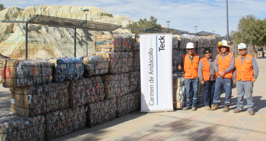 Workers stand beside compacted recyclables and a sign reading 'Carmen de Andacollo, Teck.'